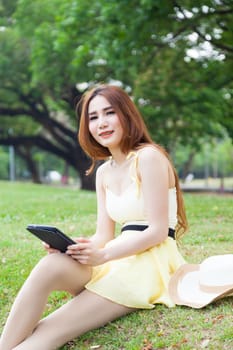 Woman sitting on lawn Hand holding tablet and thinking.