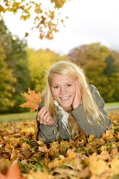 young blond woman with autumn leave lying on a meadow