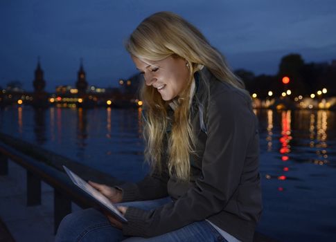 pretty young blond woman with tablet computer in the city at night