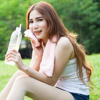 Woman is sitting a break from exercise. Sitting on the grass in the park.