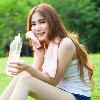 Woman is sitting a break from exercise. Sitting on the grass in the park.