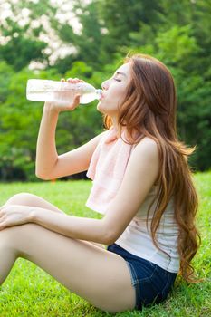 Woman sitting tired and drinking water after exercise. Within the lawn of park.