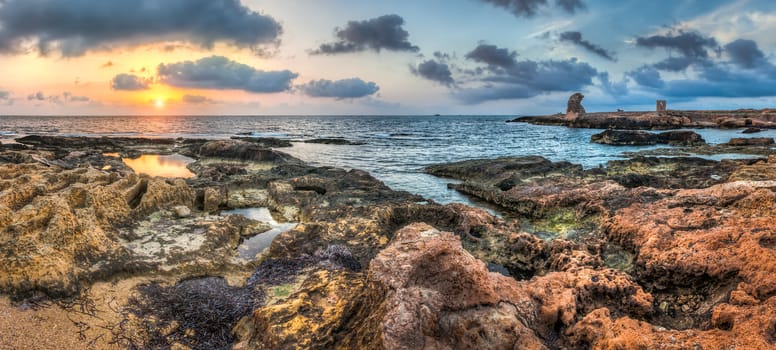 sunset over the sea and rocky coast with ancient ruins