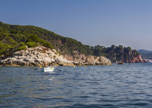 A traditional fisher paddling with his barque in a rocky cove of the Costa Brava