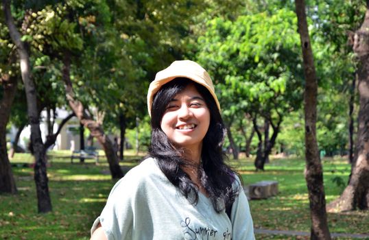 Portrait of beautiful smiling young woman in yellow hat, against background of summer green park. 