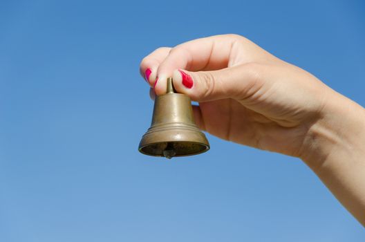 Woman hand with red nails shake small iron bell and jingle sounds on background of blue sky.