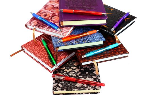 On a white background on each other are colorful notebooks and pens for writing