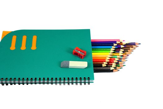 Lie on a white background notebook, sharpener, eraser and lots of colored pencils