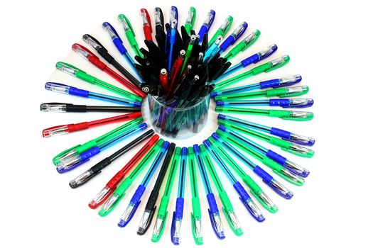 Laid out on a white background colorful pens in a circle and in the center of the glass with black handles