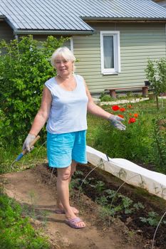 Elderly woman stands in the midst of the garden in June