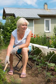 Elderly woman working in the garden, sitting on a chair