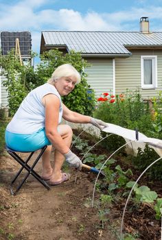 Elderly woman is engaged in weeding in the garden, sitting on a chair