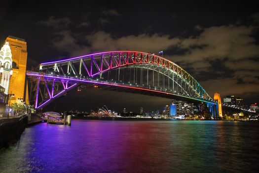 NTH SYDNEY, AUSTRALIA - JUNE 6, 2014;  Sydney Harbour Bridge in vibrant rainbow colours during the Annual Vivid Festival, view to Opera House and Circular Quay