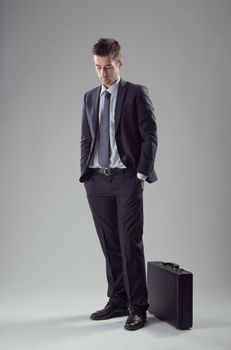 Young elegant businessman waiting with briefcase and hands in pockets.