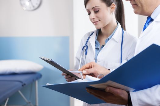 Young female practitioner and senior doctor checking medical records on a clipboard.