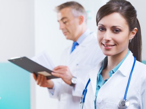 Beautiful young female doctor at hospital with collegues in the background.