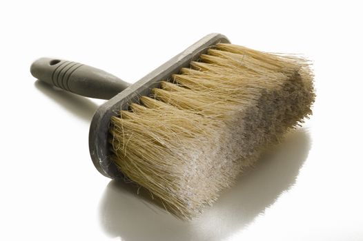 Large clean new paint brush or wallpapering brush with a plastic handle lying on a reflective white surface in a DIY, renovation and interior decoration concept
