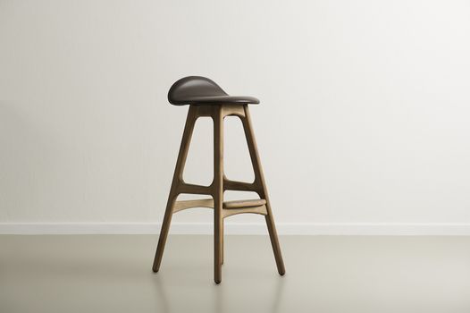 Wooden bar stool with a molded leather seat standing centered in a minimalist empty room with a white wall and copyspace, horizontal format