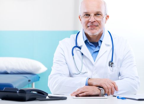 Senior doctor at his desk working with medical equipment in the background.