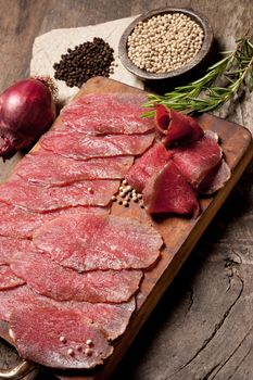 Slices of meat with spices and onions on wooden board.