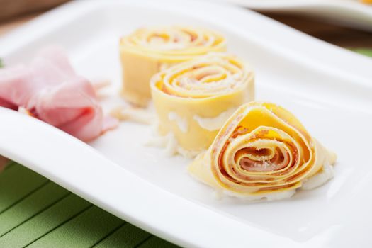 Fresh pasta rolls with ham and sauce on square plate.