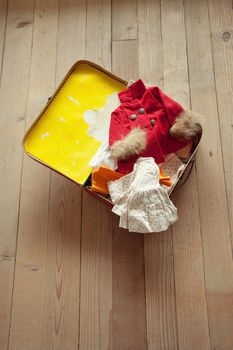 Open vintage suitcase with folded clothing on hardwood floor.