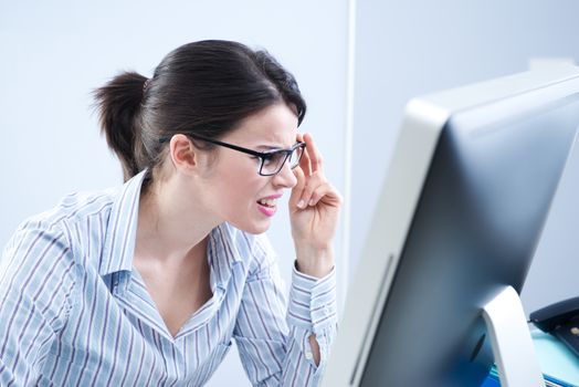 Young office worker staring at computer screen and adjusting glasses.