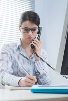 Woman working on the phone and writing down notes at office.