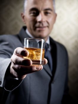 Businessman holding a glass of whisky with vintage wallpaper background.