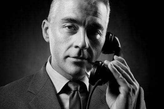 Handsome man holding a vintage phone receiver on dark background.
