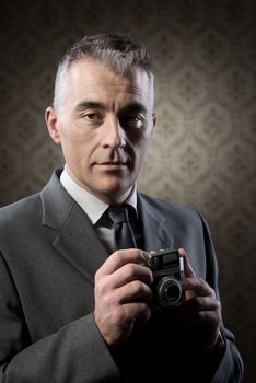 Handsome photographer shooting with vintage camera against retro wallpaper.