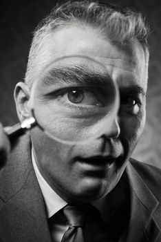 Vintage detective looking at camera through magnifying glass.