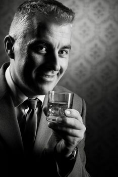 Businessman holding a glass of whisky with vintage wallpaper background.