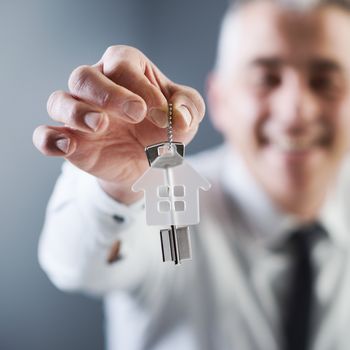 Real estate agent holding out keys of your new house.