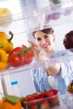 Young woman taking fresh healthy vegetables from refrigerator.