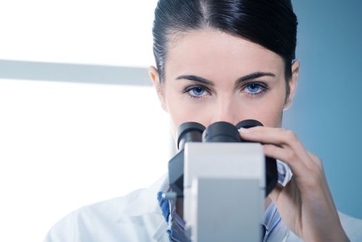 Attractive female researcher using microscope and looking at camera.