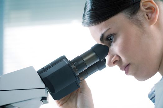Young female researcher using microscope in the laboratory close up.