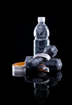 Water bottle, measure tape and dumbbells on black background.