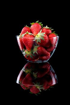 Delicious strawberries in a glass bowl on black background.