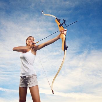 Attractive woman aiming with bow and arrow with blue sky on background.