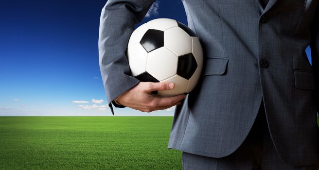 Businessman holding a soccer ball with blue sky and green meadow on background.