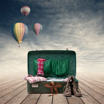 Explorer's suitcase with clothing and boots, hot air balloons on background.