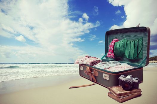 Open suitcase with old books and camera with seaside and blue sky on background.