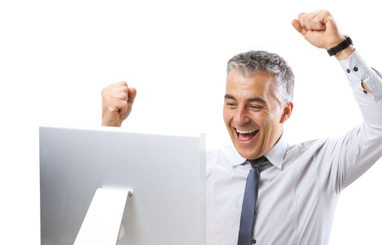 Mature businessman receiving good news on computer with fists raised.