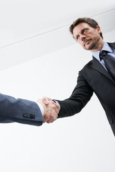Confident businessmen shaking hands with empty white room on background.