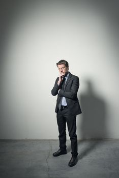 Pensive businessman with hand on chin standing in an empty room with dramatic lighting.