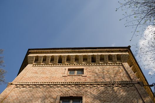 red brick manor architectural fragment with small windows and ornaments on blue sky background