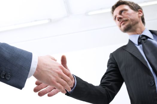 Confident businessmen shaking hands with empty white room on background.