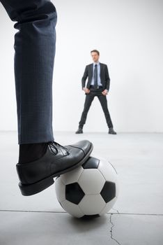 Businessmen playing soccer in an empty room, ball and foot close up with goalkeeper on background.
