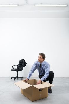 Pensive businessman looking around and packing with cardboard box in an empty office.